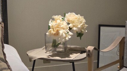 Elegant cream flowers arranged in clear square vase placed on small table in cozy room