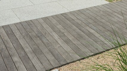 Fototapeta premium Wooden deck pathway combined with stone tiles and gravel creating a modern outdoor landscape design.