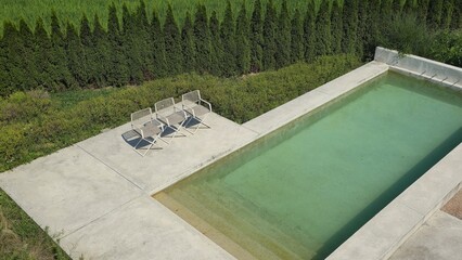 Modern outdoor pool with clean concrete deck, minimalist chairs, and lush green landscape offering a serene and relaxing atmosphere.