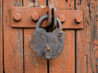 Old rusty padlock locks light brown wooden gate with peeling paint close-up