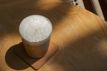 a glass of iced milk coffee on wooden table in sun light and shade