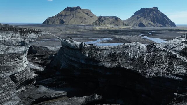 Aerial view of gray rock formations contrasting with distant mountains under a clear sky, creating a stark yet compelling landscape, Iceland.