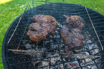 Grilled pork steaks sizzling on a charcoal barbecue grill. Juicy meat cooking outdoors on a summer day for a backyard BBQ party. Perfect outdoor cooking scene with smoky flame-grilled meat steaks