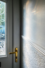 Brass handle on white front door with textured stained glass and prism light on interior wall