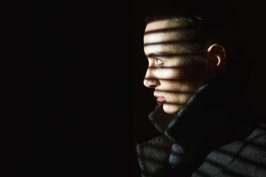 Detective in striped shadow with contemplative expression in noir setting