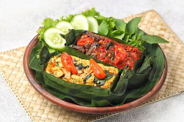 Nasi bakar daun or grilled rice on banana leaves isolated on cement background. This rice is wrapped by using banana leaf and then roasted by using charcoal. Ingredients with seafood, meat, chicken
