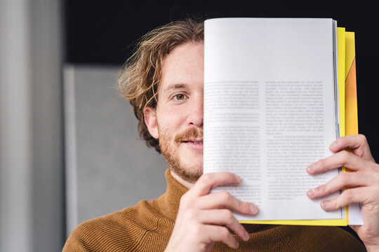 Author holding magazine in modern home loft smiling at camera