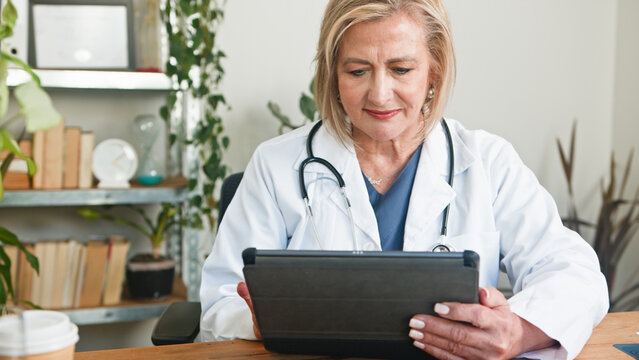 Senior Female Doctor Using Tablet in Office with Medical Instruments
