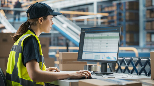 Caucasian Female Stocking Associate Using Desktop Computer To Check Inventory In Distribution Facility. Warehouse Worker Checking Orders on Automated Conveyor Belt - Powered by Adobe