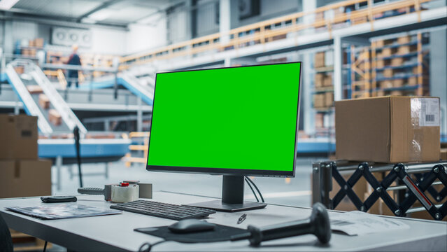 Empty Workplace of Sorting Center Employee With Green Screen Chromakey Desktop Computer Monitor And Barcode Reader. Conveyor Belt With Online Orders Packaged In Cardboard Boxes Working On Background. - Powered by Adobe