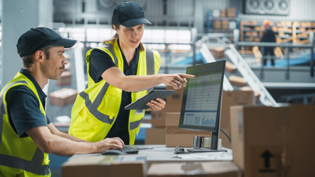 Caucasian Male Stocking Associate Using Desktop Computer, Talking to Female Supervisor With Tablet In Warehouse With Conveyor Belt. Man And Woman Working In Sorting Center of Online Marketplace. - Powered by Adobe