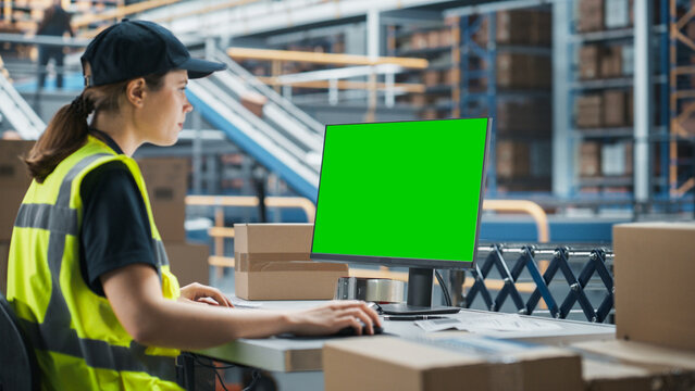 Caucasian Female Stocking Associate Using Green Screen Chromakey Desktop Computer In Distribution Warehouse. Male Colleague Loading Cardboard Boxes On Automated Conveyor Belt In Sorting Center