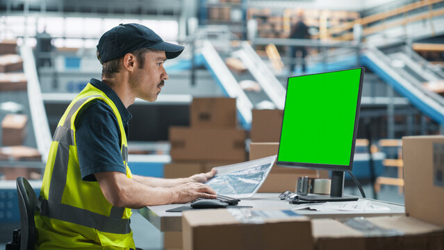 Caucasian Male Stocking Associate Using Green Screen Chromakey Desktop Computer In Distribution Facility. Multiethnic Male Warehouse Worker Scanning Barcodes On Cardboard Boxes WIth Online Orders. - Powered by Adobe
