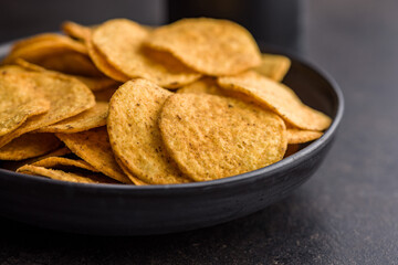 Crispy potato chips in bowl on black table.