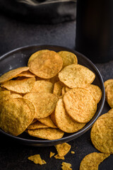Crispy potato chips in bowl on black table.