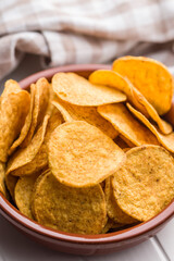 Crispy potato chips in bowl on white table.