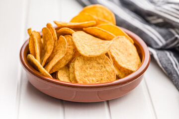 Crispy potato chips in bowl on white table.