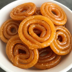 Fototapeta premium Golden spiral sweet jalebi dessert in a white bowl