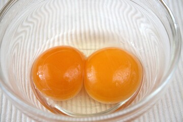 A close-up view of two raw egg yolks inside a transparent glass bowl. Ideal for cooking or food preparation themes.