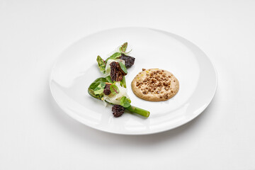 A fine dining dish featuring a savory paté topped with crunchy elements, served with a delicate salad of asparagus and microgreens on a white plate.
