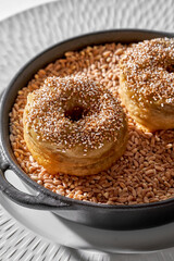 Two creative savory doughnuts with meat rillette and crunchy topping, served on a bed of grain in a cast iron skillet
