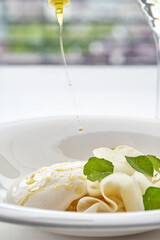 A fine dining dish with fresh pasta, a creamy cheese ball, and delicate herbs, drizzled with olive oil, served in a minimalist white bowl.