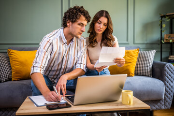 Couple discussing home finance while checking bills. They are checking financial documents and calculating family budget in living room.