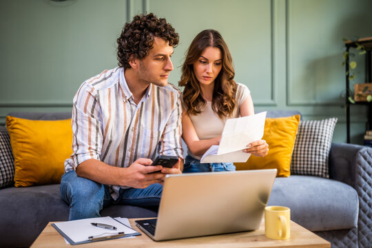 Couple discussing home finance while checking bills. They are checking financial documents and calculating family budget in living room.