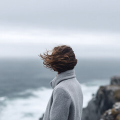 Woman gazing at the stormy sea, wind blowing through her hair. Serene solitude, introspection, and resilience. Perfect for travel, lifestyle, or personal growth content.