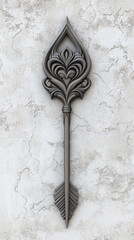 Decorative metal arrow with intricate floral design mounted on cracked white wall, showcasing elegant craftsmanship and vintage style