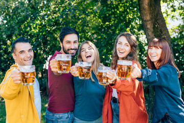 Happy friends toasting with beer mugs in garden party