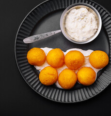 Savory golden balls served with creamy dipping sauce on a black plate
