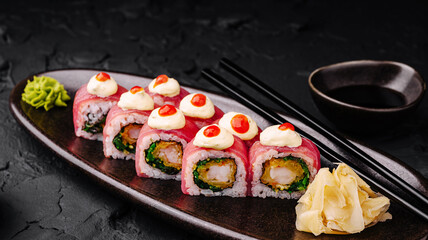 Fresh sushi rolls arranged on a black plate with garnishes and dipping sauce
