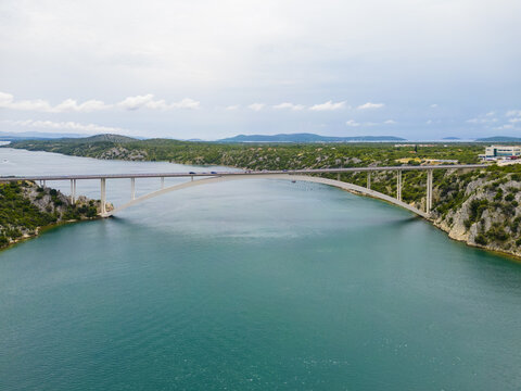 Aerial view of a bridge arcing gracefully over the turquoise waters, connecting verdant shores under a vast, cloudy sky, Skradin, Sibensko-kninska &Aring;&frac34;upanija, Croatia.