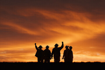 Fototapeta premium Silhouette of determined workers against a fiery sunset. Symbolizing strength, unity, and triumph. Ideal for themes of teamwork, resilience, and overcoming challenges.