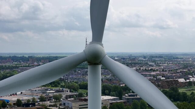 Pull-back, drone footage of a wind turbine spinning above a suburban polder area in the Netherlands