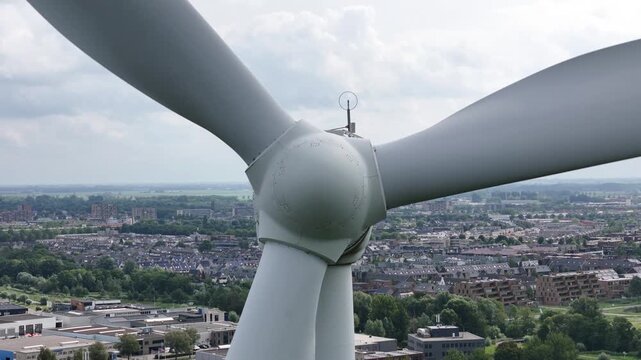 Closeup, drone footage of a wind turbine spinning above a suburban polder area in the Netherlands