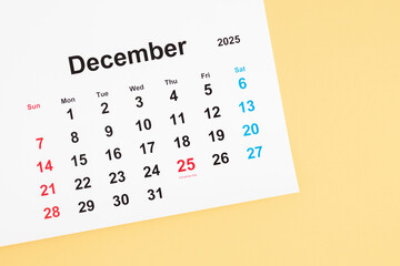 Top view of December 2025 calendar with date 25 marked, Christmas celebration on light yellow background