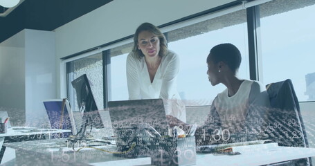 Collaborating professional women analyzing documents on laptops at office desk, with data overlay