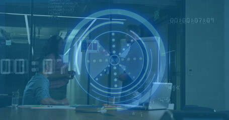 Manipulating circular interface above conference table in room, typing on laptop and holding tablet