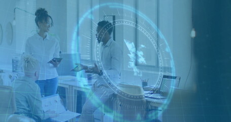 Discussing office colleagues sharing ideas in open-plan workspace, with laptops, tablet, smartphone