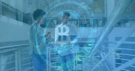 Colleagues holding smartphone and laptop discussing Bitcoin in office atrium, with Bitcoin hologram