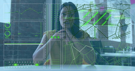 Analyzing data overlays by mature woman sipping from coffee mug at office desk, with map interfaces
