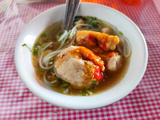 Meatball. A bowl of meatballs complete with yellow noodles, crispy fried dumplings, etc., served with delicious thick sauce on the table.
