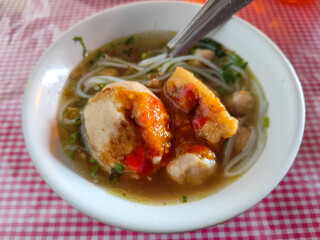 Meatball. A bowl of meatballs complete with yellow noodles, crispy fried dumplings, etc., served with delicious thick sauce on the table.
