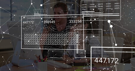 Adult Asian analyst analyzing data overlays at desk in office, with dual monitors and keyboard
