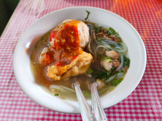 Meatball. A bowl of meatballs complete with yellow noodles, crispy fried dumplings, etc., served with delicious thick sauce on the table.