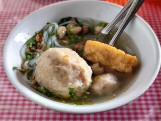 Meatball. A bowl of meatballs complete with yellow noodles, crispy fried dumplings, etc., served with delicious thick sauce on the table.
