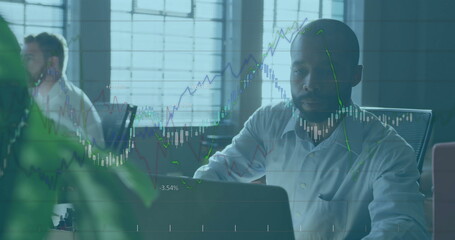 Analyzing man viewing market charts on laptop screen in open-plan office, with potted green plant