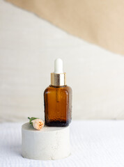 An elegant bottle in noble dark glass with natural serum and the most delicate cream to brighten your skin is decorated with an elegant flower on a plaster catwalk.